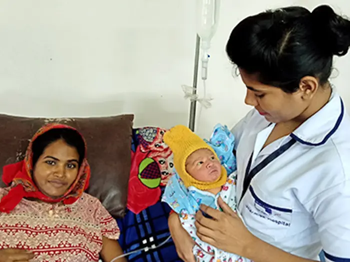 A newborn baby held by a health worker with the mother close by smiling.