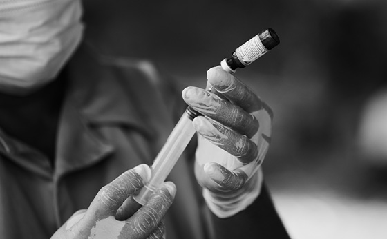 Black and white photo of a health worker preparing a vaccine syringe.
