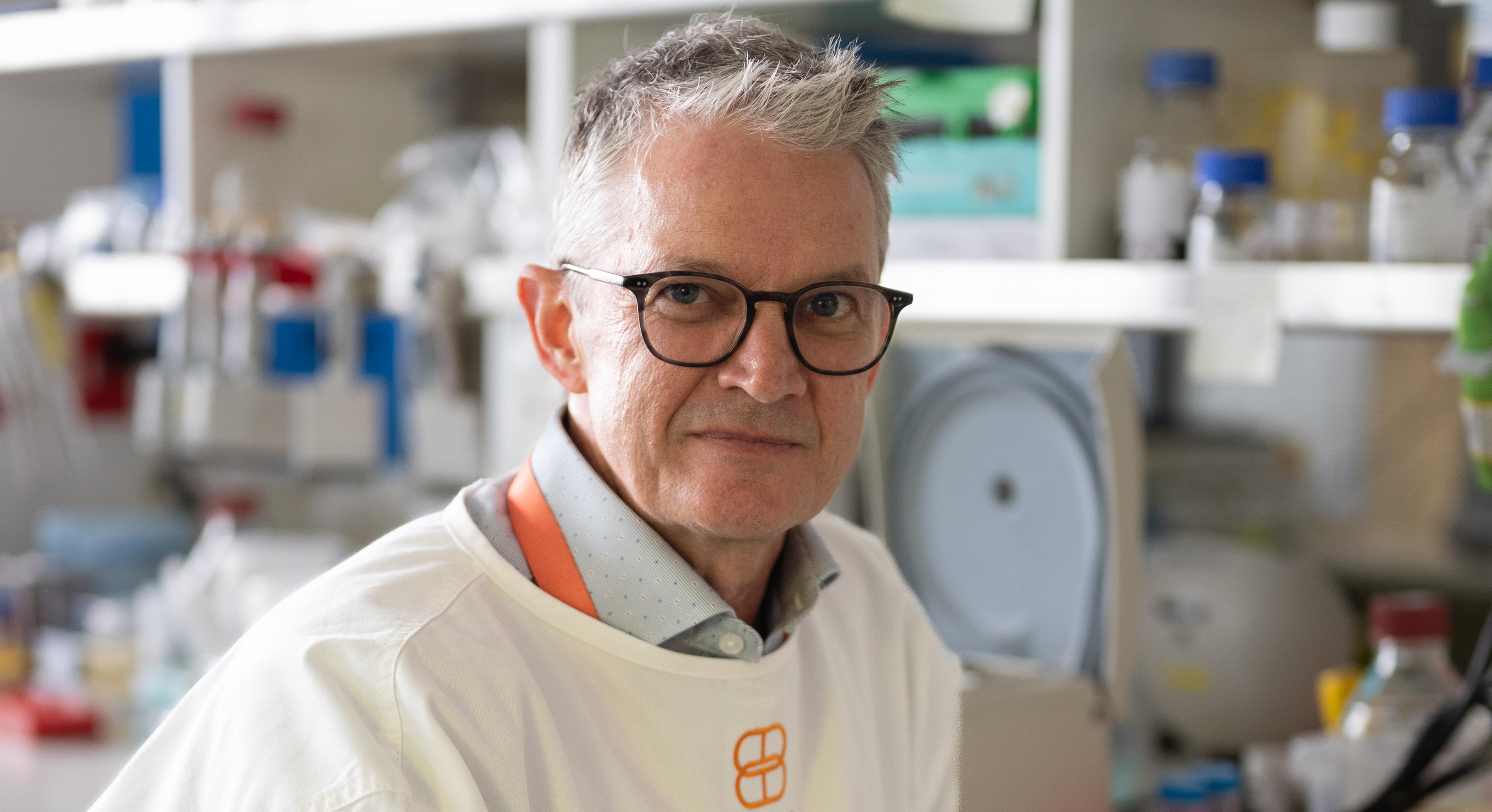 Brendan Crabb, in a lab, wearing a lab coat and gloves.