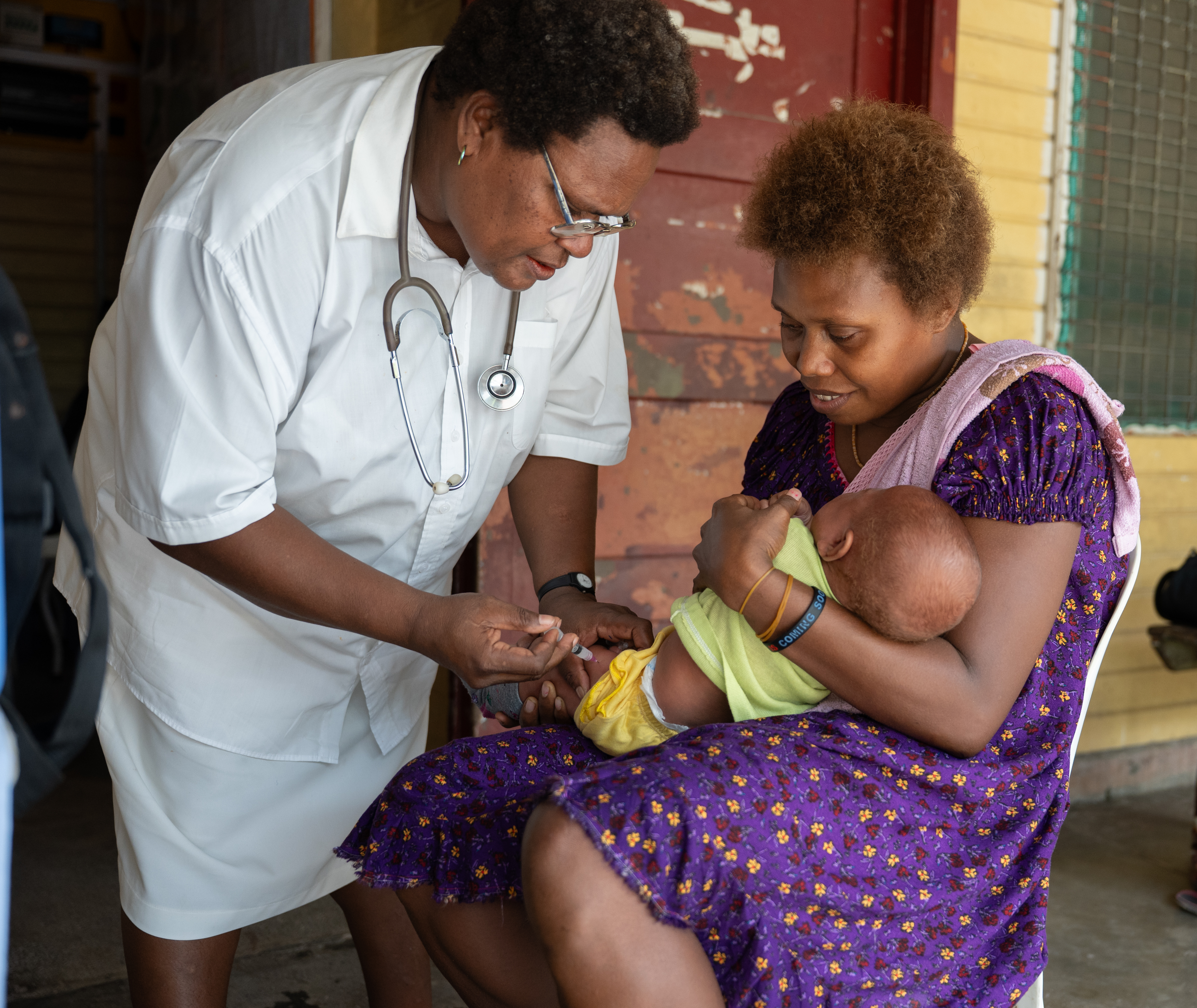 Healthcare worker giving a baby an injection while the mother holds the child.