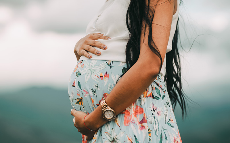 Woman with long black hair holding her pregnant belly.