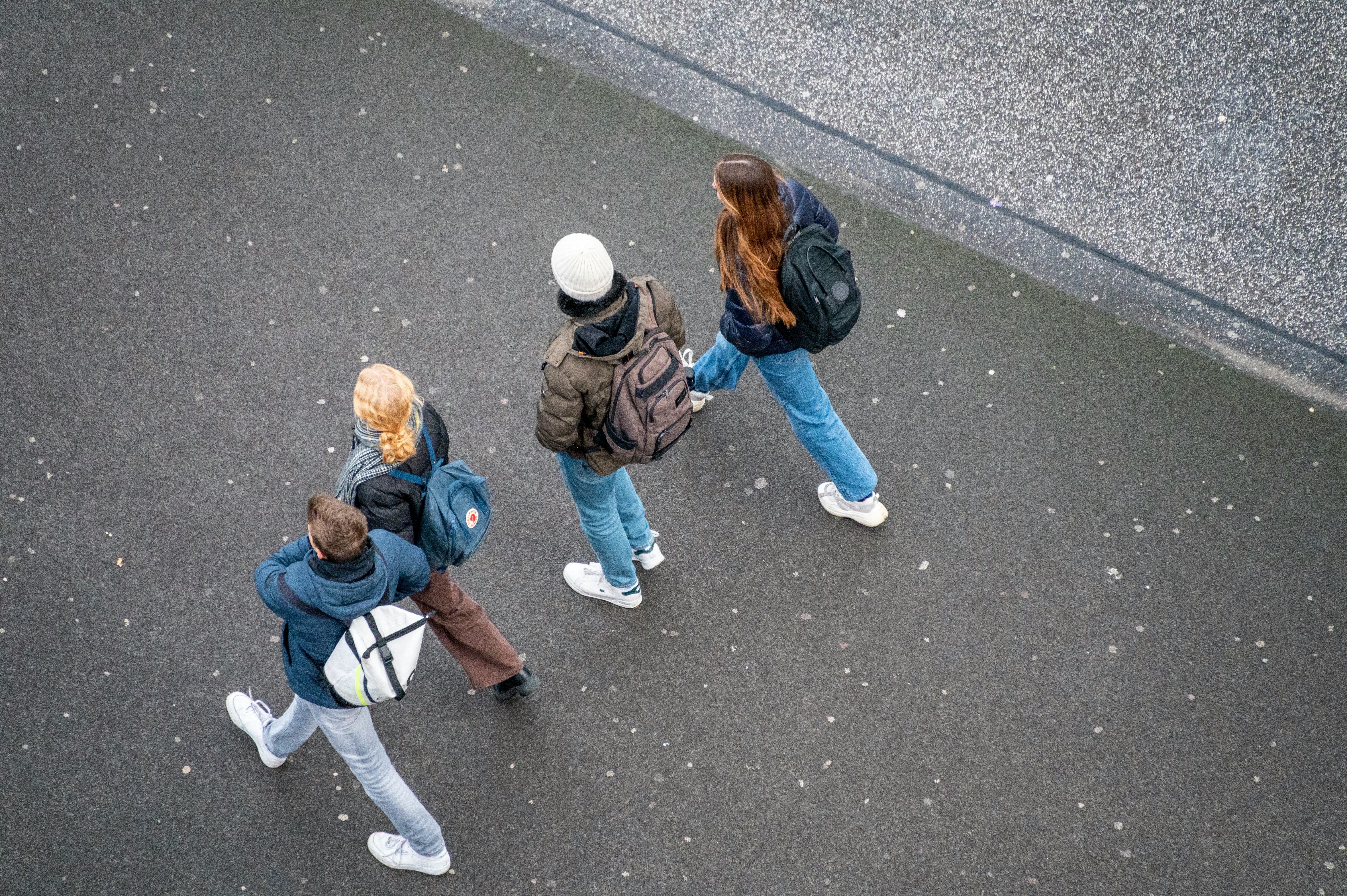 Four young people walking, carrying backpacks on a sidewalk.