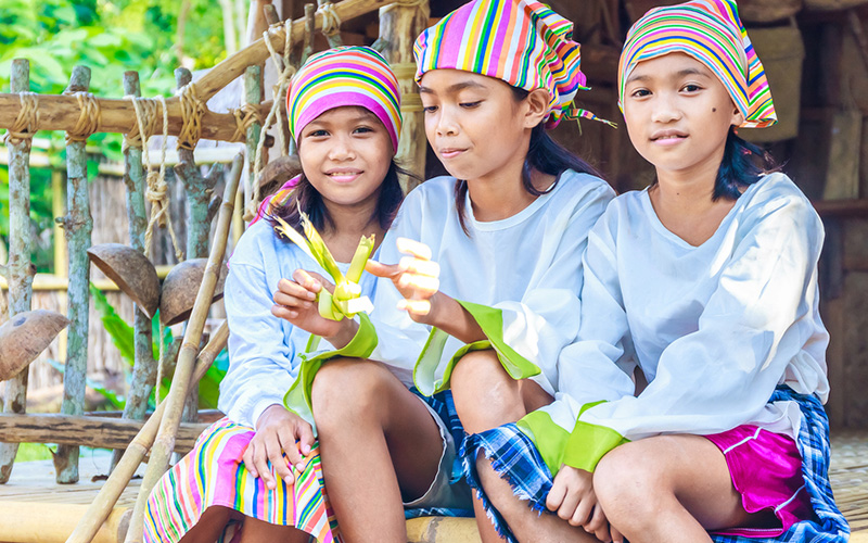 Girls in traditional clothes in bamboo house making toys from palm leaves in the Philippines.