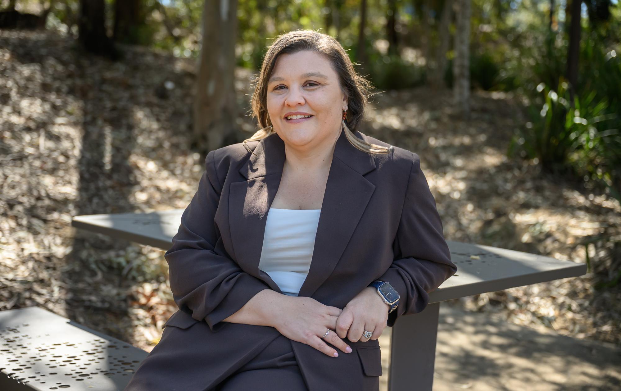 Stacey Butcher sits on a picnic bench in a forest. 