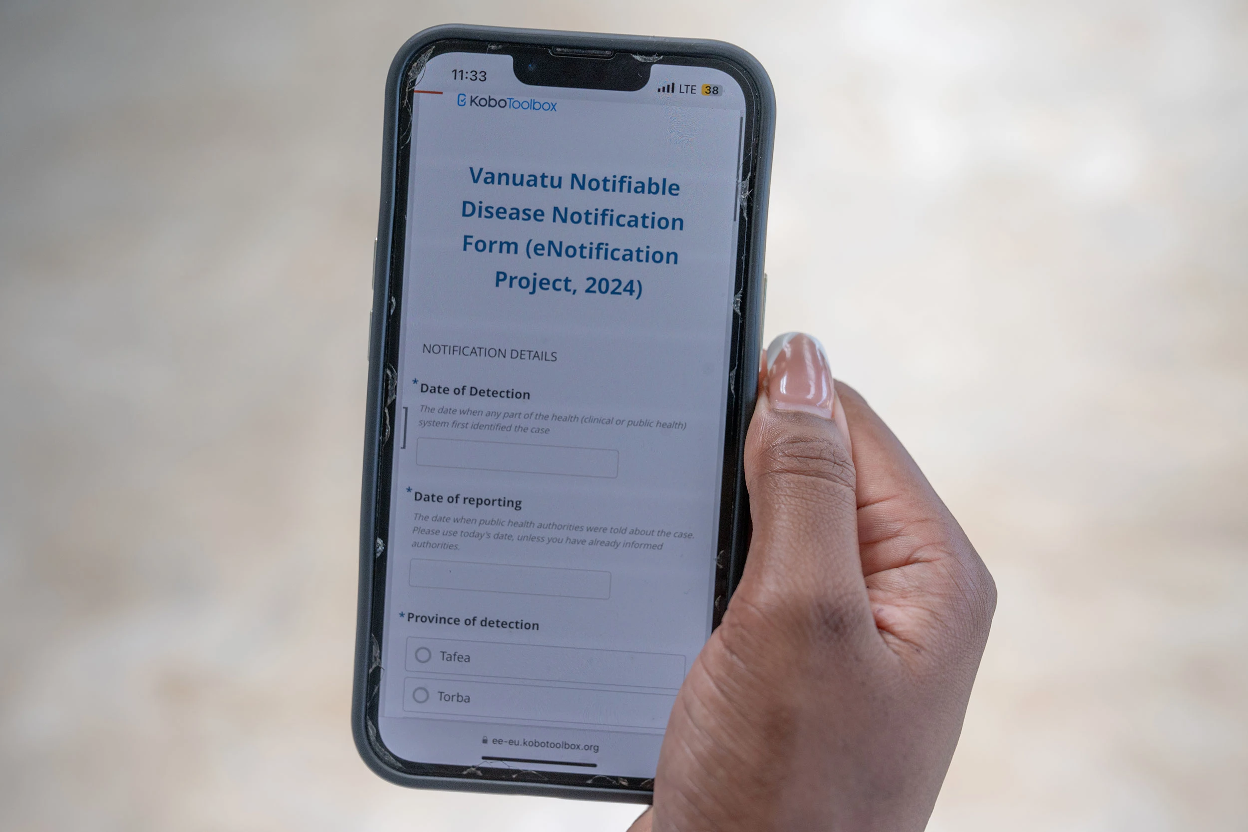 A mobile phone is held in someone's hand. The screen has a form on it that reads "Vanuatu Notifiable Disease Notification Form"