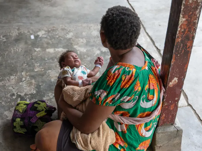 An infant is held by someone facing away from the camera, in Paparatava Health Outpost, East New Britain.