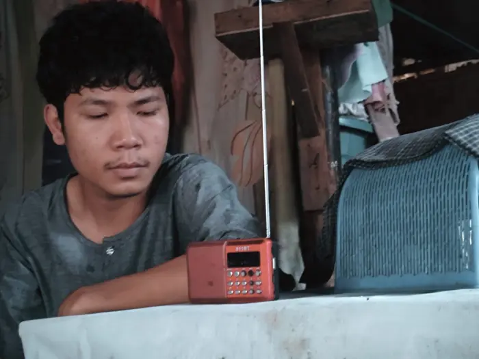 Aung Aung feeling distressed, looking at the radio.