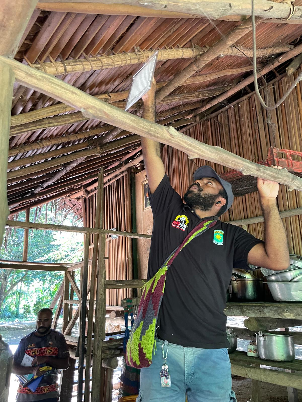 A staff member hanging up a paper-sized white plastic casette on a wooden beam in an open-air building.
