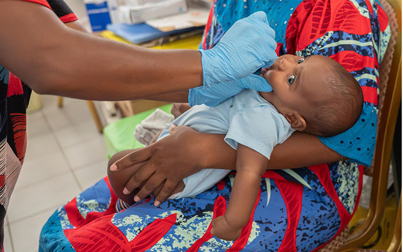 A baby in a person's arms receiving an oral vaccination from a person wearing medical glovesl.