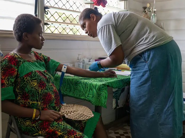A health worker draws blood from a patient in a consulting room.