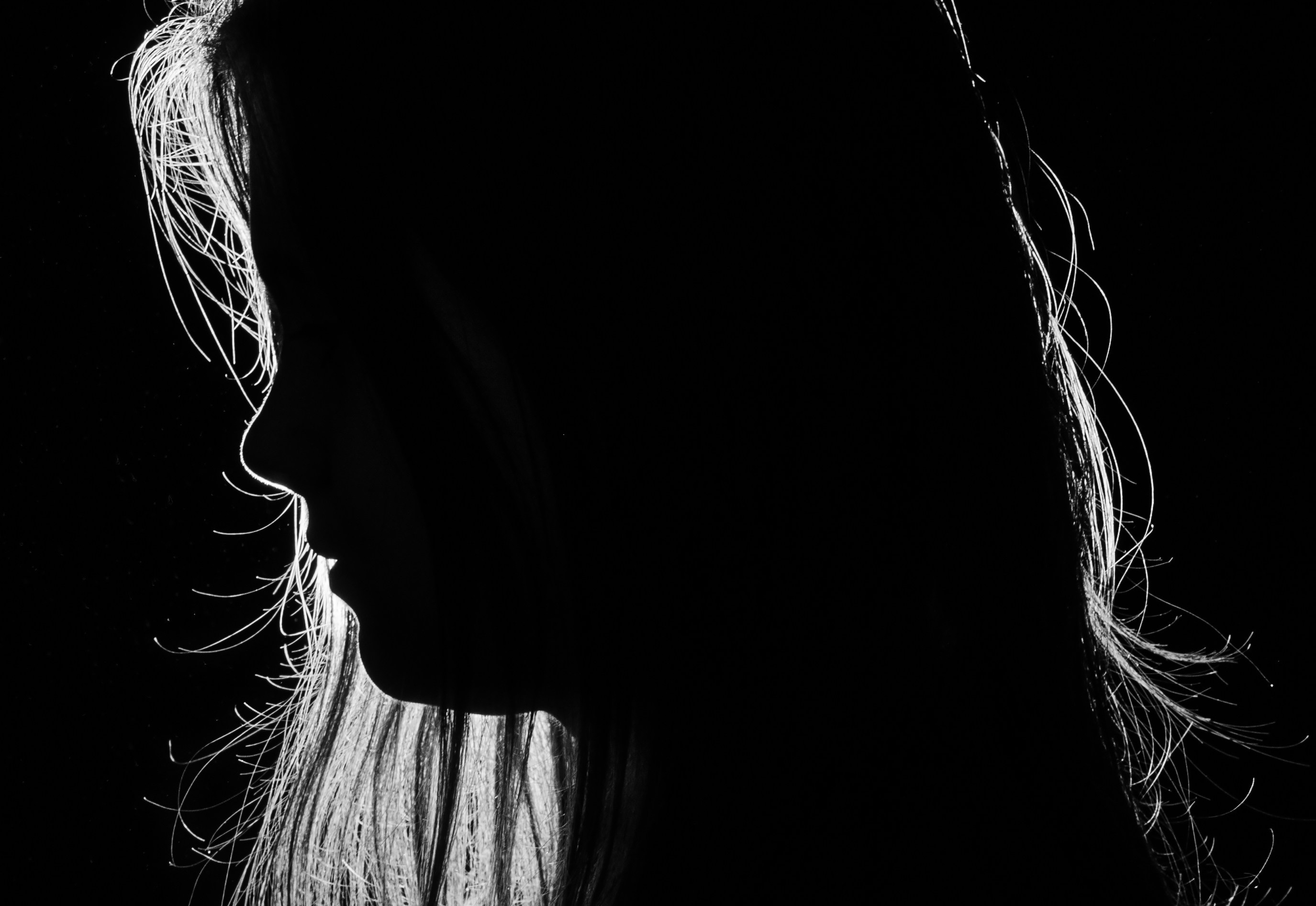 Silhouette of a woman in side profile against a dark background, with light outlining the edges of her face and long hair.