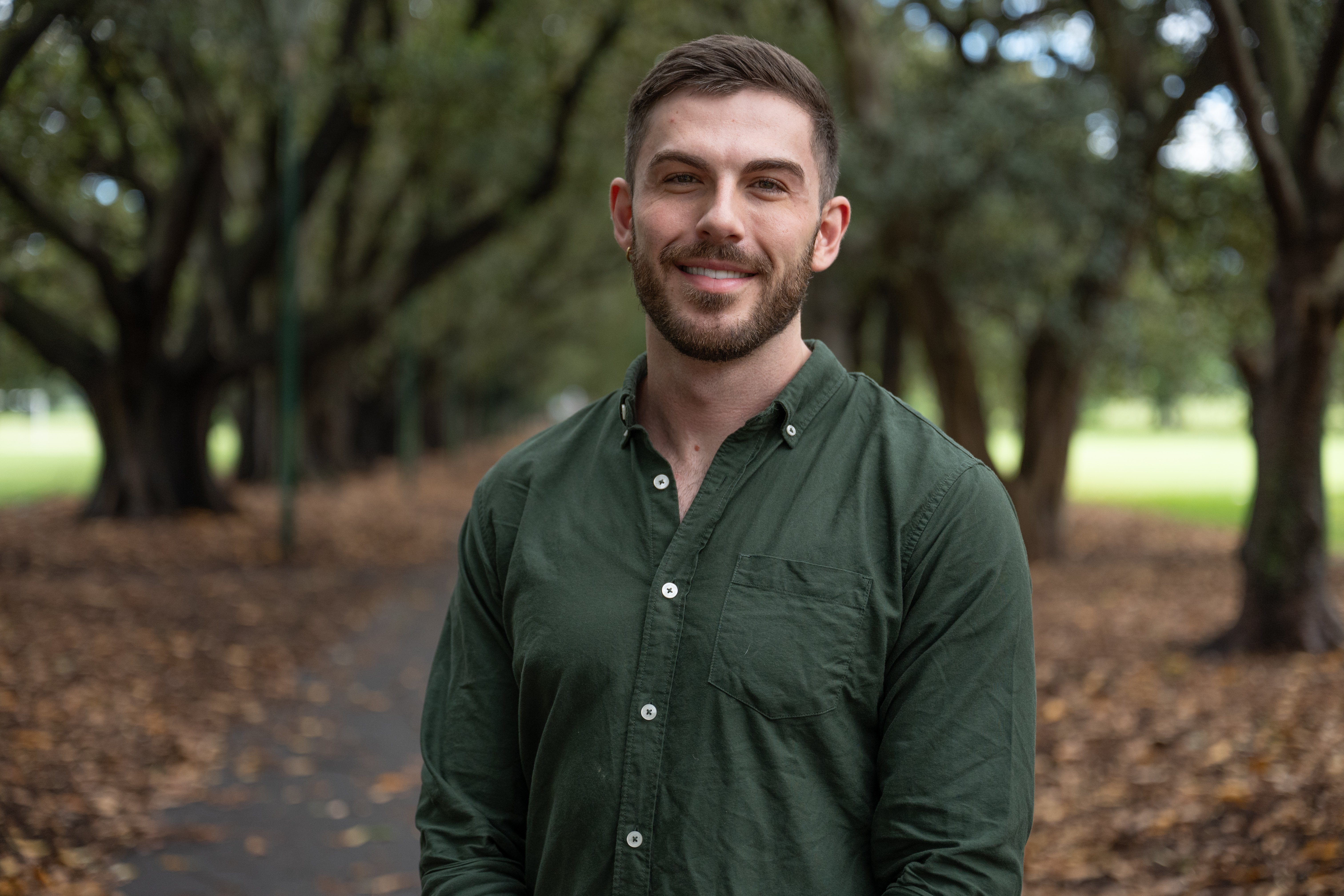 Michael Traegar, a man wearing a green button up shirt, standing and smiling at a park.