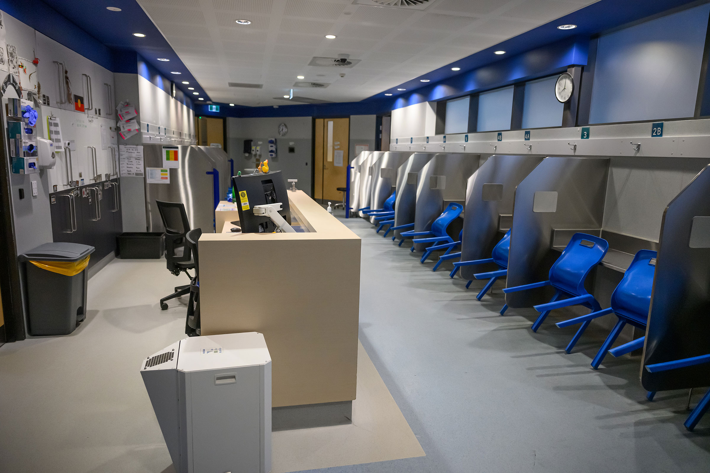 Interior of a supervised injecting room. A reception desk is in the foreground and there are chairs and stalls in the background. 