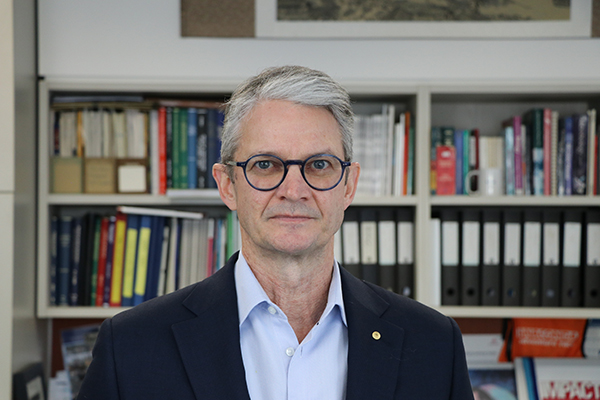 Brendan Crabb, wearing glasses, looking at the camera, standing in front of a bookshelf.