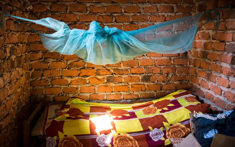 A blue mosquito net hangs above a bed in a dimly lit room.